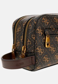 Bolso con patrón marrón y negro, herrajes en tono dorado, dos cierres de cremallera y un asa de cuero marrón. Presenta un diseño de logotipo grabado en el material.