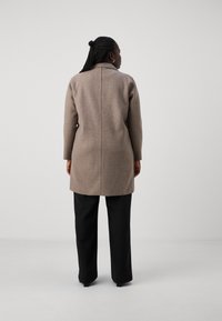 Manteau en mélange de laine taupe, coupe droite, manches longues et détail de couture au dos. Associé à un pantalon large noir.