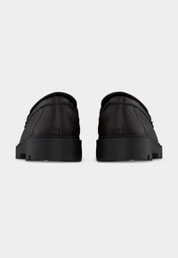 Ζευγάρι σκούρα καφέ δερμάτινων μοκασίνων με μαύρες χοντρές λαστιχένιες σόλες, φωτογραφημένα από πίσω με φόντο ένα απλό λευκό φόντο.