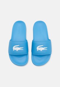 Sandales en caoutchouc bleu avec une large bride arborant un logo de crocodile blanc, texture lisse et forme arrondie pour le confort.