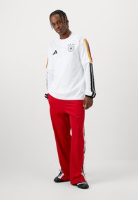 Hvit langermet skjorte med svarte og røde striper, med et logo og tre stjerner. Røde bukser med svarte sidestriper og logoer.