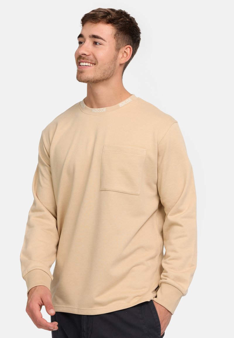 Beige langærmet skjorte med rund hals. Har en brystlomme og logo-detalje på kraven. Glat tekstur med en afslappet pasform.