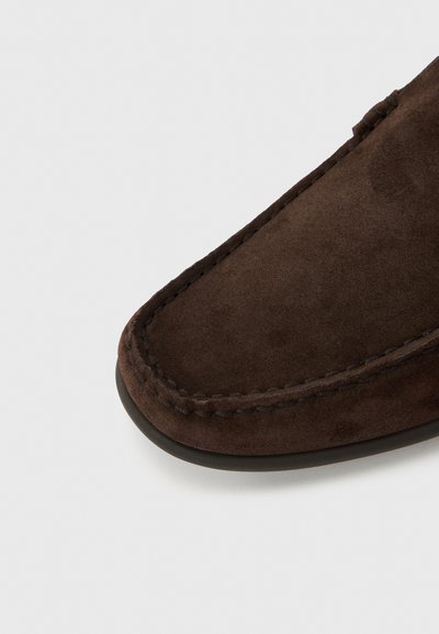 Chausson en daim marron à texture lisse, forme arrondie et couture contrastante. Design à enfiler avec une semelle extérieure flexible.