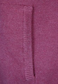 Část pletené látky v barvě šeříku s boční kapsou s texturovaným okrajem a žebrovaným detailem kolem otvoru kapsy.