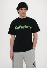 Tricou negru din bumbac, cu text verde "NoProblemo". Mâneci scurte, design cu guler rotund, croială lejeră. Textură netedă, stil minimal.