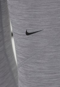 Harmaat urheiluhousut, joissa on teksturoitu kuvio, musta Nike-logo sivulla ja näkyvät ompelusaumat.