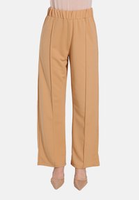 Bredde ben, beige bukser med elastisk talje, glat tekstur og lodrette sømme; parret med beige spidse hæle.