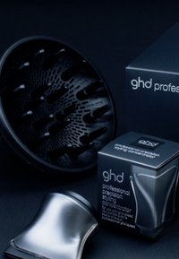 Diffuseur de cheveux noir et embout concentrateur de coiffage argenté à côté de boîtes d'emballage noires avec le logo "ghd professional".
