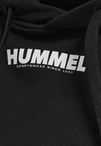 Czarna bluza z kapturem wykonana z miękkiej tkaniny, z białym nadrukowanym logo "HUMMEL SPORTSWEAR SINCE 1923" wokół dekoltu.