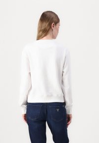 Felpa bianca in cotone con maniche lunghe, scollo a girocollo e polsini a coste, abbinata a jeans di denim blu scuro con tasche posteriori e dettagli.