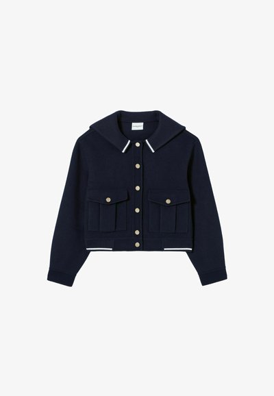 Chaqueta recortada azul marino hecha de tela suave con un amplio collar, botones de presión dorados y dos bolsillos frontales. Presenta acentos a rayas blancas en los puños.