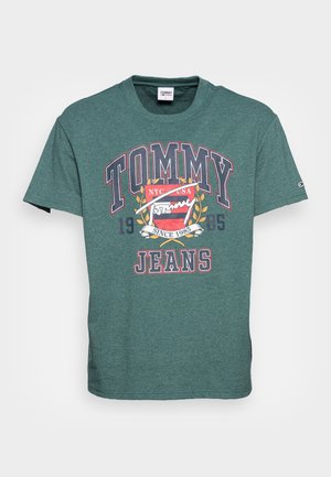 Grøn kortærmet Tommy Jeans t-shirt med stort logo foran, våbenskjold og tekst med "NYC USA Since 1985" på hvid baggrund.