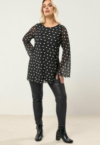Tunic nera con pois bianchi, maniche lunghe trasparenti e orlo scallop. Abbinata a pantaloni in pelle nera aderenti e stivaletti.