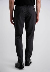 Zwarte broek met patroon en een getailleerde pasvorm, met zij- en achterzakken, gecombineerd met zwarte formele schoenen. Vlakke textuur en subtiel ontwerp.
