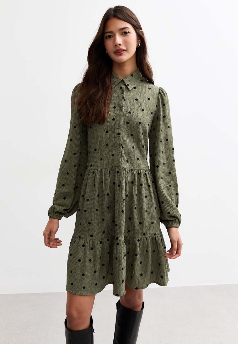 Robe verte en tissu texturé, dotée d'un col, de longues manches bouffantes et de pois noirs. Détail d'ourlet en niveaux.