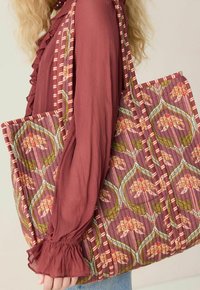 Sac fourre-tout matelassé en prune profond avec des motifs floraux et de feuilles, accentué par des rayures étroites. Tissu doux avec un design texturé.