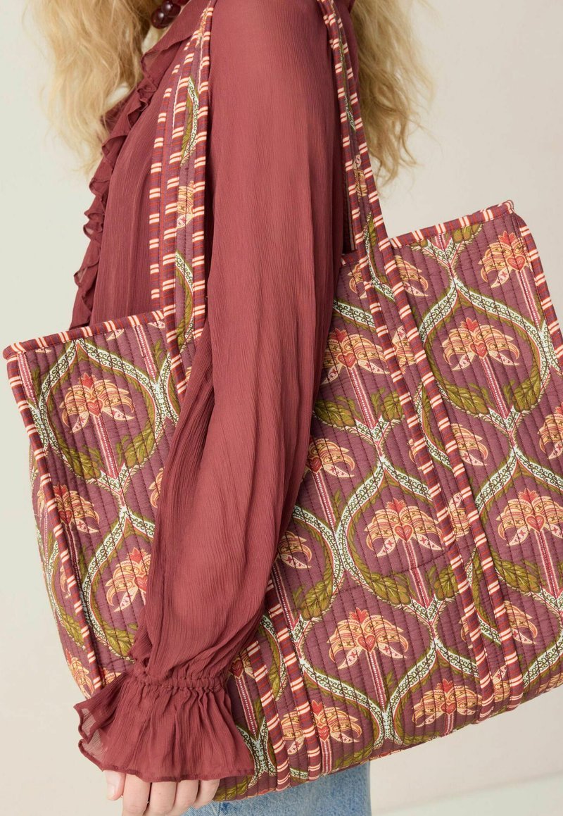 Sac fourre-tout matelassé en prune profond avec des motifs floraux et de feuilles, accentué par des rayures étroites. Tissu doux avec un design texturé.