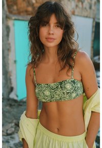 Žalias gėlių bikini viršus su plonomis petnešėlėmis, turintis kvadratinį dekoltė. Sujungtas su šviesiai geltonais laisvais šortais ir per dideliu marškiniais.