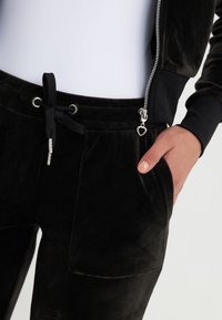 Svarta velour joggers med en mjuk textur, som har dragsko i midjan, sidofickor och en dragkedjedetalj med ett hjärtformat hänge.