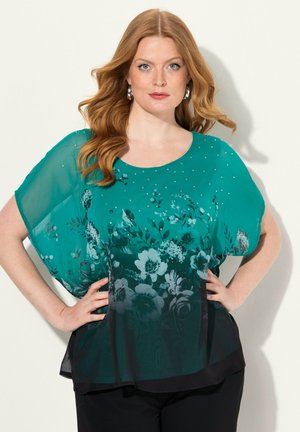 Blusa floreale color turchese in tessuto trasparente, caratterizzata da intricati motivi floreali, sottili paillettes e una vestibilità ampia, abbinata a pantaloni neri.