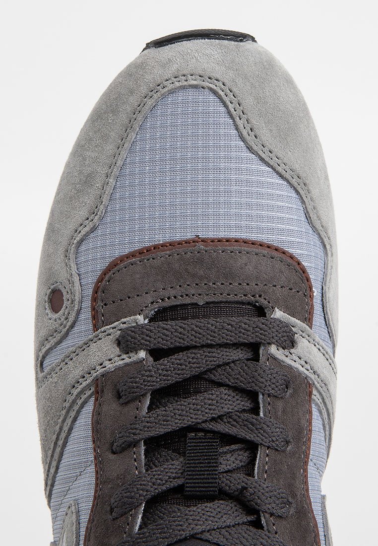 Grijze suede en blauwe mesh sneaker met donkergrijze veters, voorzien van bruine accenten en een gestructureerd patroon op de bovenkant.