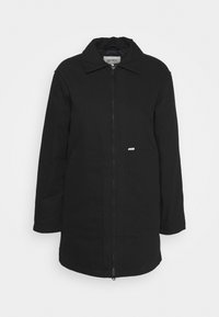 Sort jakke med krave, lynlås foran, to lommer og lange ærmer. Materialet fremstår glat med en mat overflade. Har minimal branding.