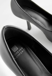 Czarne skórzane buty na wysokim obcasie o eleganckim designie i gładkiej fakturze, z wnętrzem oznaczonym marką "Forever Comfort."