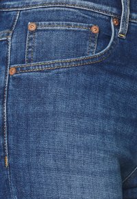 Jeans de mezclilla en un lavado azul medio, con herrajes de cobre, costuras tonales y un clásico diseño de cinco bolsillos con un pequeño bolsillo frontal.