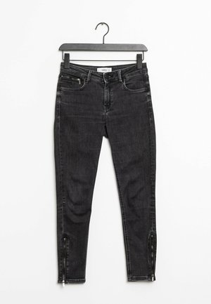 Vaqueros negros ajustados con una textura suave, con un detalle de cremallera en el tobillo, bolsillos frontales y una cintura de altura media.