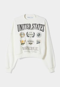 Biała krótka bluza z nadrukowanym czarnym tekstem, wieloma kolorowymi naszywkami i ściągaczami. Miękka tkanina i luźny krój.