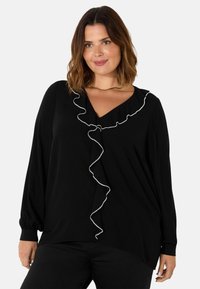 Blusa nera con maniche lunghe, scollo a V e una linea fluida. Presenta un bordo arricciato bianco lungo il décolleté e maniche leggermente gather.
