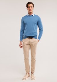 Maglione azzurro chiaro sopra una camicia con colletto, chinos beige e sneaker crema. Tessuto morbido, design aderente e branding sottile sui pantaloni.