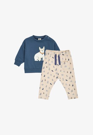 Blaues Langarm-Toddler-Shirt mit weißem Hundegrafik, kombiniert mit beigen Hosen mit kleinen Hundemustern und einer dunkelblauen Kordel.