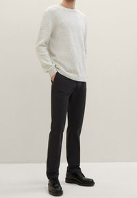 Maglione grigio chiaro a girocollo con un tessuto lavorato, abbinato a pantaloni neri slim-fit e scarpe nere stringate.