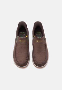 Ζευγάρι καφέ casual παπουτσιών slip-on με ύφασμα mesh και λευκές σόλες, με το λογότυπο John Deere στο πάνω μέρος.