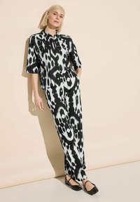 Svartvit m�önstrad jumpsuit med korta ärmar, knapp-up front, matchande bälte och lös passform. Buren med svarta balett flat-sandaler.