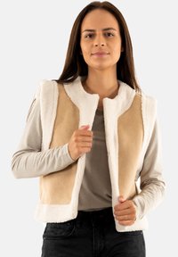 Chaleco sin mangas en color beige y crema, confeccionado con una tela suave y esponjosa con un acabado texturizado. Presenta un escote redondo y un diseño de frente abierto.