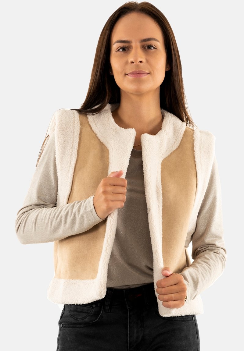 Chaleco sin mangas en color beige y crema, confeccionado con una tela suave y esponjosa con un acabado texturizado. Presenta un escote redondo y un diseño de frente abierto.