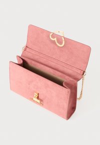 Borsa in suede rosa con patta a forma di cuore dorata, tracolla a catena e un accento con logo. L'interno è foderato in tessuto beige.