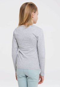 Graues Langarmshirt aus leichtem Stoff, kombiniert mit hellblauen Hosen. Es hat einen runden Ausschnitt und eine weiche Textur, mit minimalen Details.