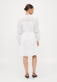 Vestido branco com mangas compridas e detalhes em renda, inclui uma cintura ajustada e bainha franzida, feito de tecido leve.