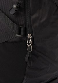 Black backpack featuring textured fabric, a prominent zipper with a silver pull, and adjustable straps. Includes a side mesh pocket.