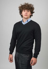 Černý pletený svetr s výstřihem do V, dlouhými rukávy a žebrovanými manžetami, nošený přes světle modrou košili s knoflíky, v kombinaci s tmavými džíny.