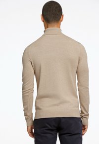 Suéter de cuello alto de punto beige, ajuste slim, mangas largas, puños y dobladillo acanalados, textura suave, con detalle de etiqueta lateral.