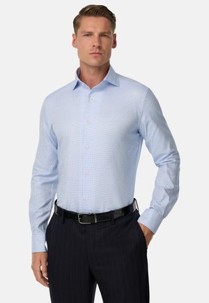 Camicia azzurra con bottoni, con un motivo testurizzato, maniche lunghe e colletto, indossata con pantaloni scuri a righe sottili e una cintura nera.