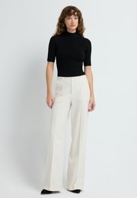 Czarny, prążkowany top z krótkim rękawem i wyższym kołnierzem, zestawiony z białymi spodniami typu wide-leg na wysokim stanie, z subtelnymi prążkami. Klasyczne czarne obuwie dopełnia całość.