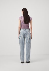 Lila, genomskinlig topp med kort ärm och figurnära design. Ljusblå, vida jeans med fickor och patch-logotyp på baksidan.