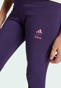 Lila leggings i en bomullsblandning med röda Adidas- och Disney-logotyper. Mjuk textur med figurnära design och slät finish.