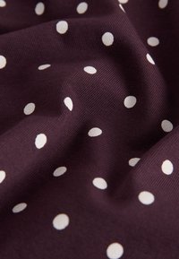 Dark purple fabric with scattered white polka dots, showing soft folds and textured weave details.