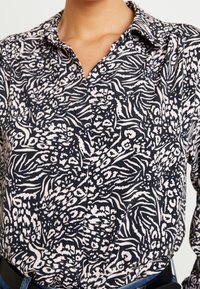 Button-up shirt in navy with a contrasting white abstract floral and zebra pattern. Features a collar and long sleeves, made from soft fabric.
